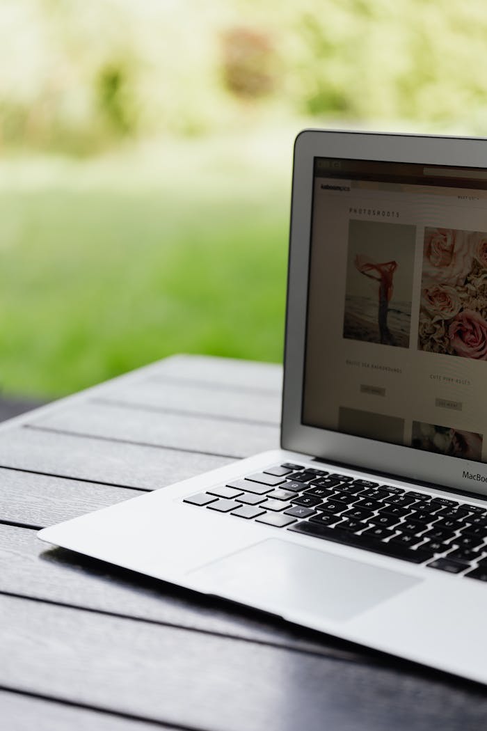 Close-up of an open laptop on a table displaying a website outdoors.